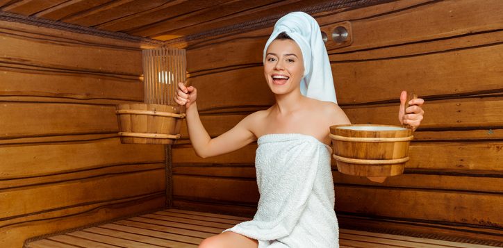 smiling-and-attractive-woman-in-towels-holding-washtubs-in-sauna