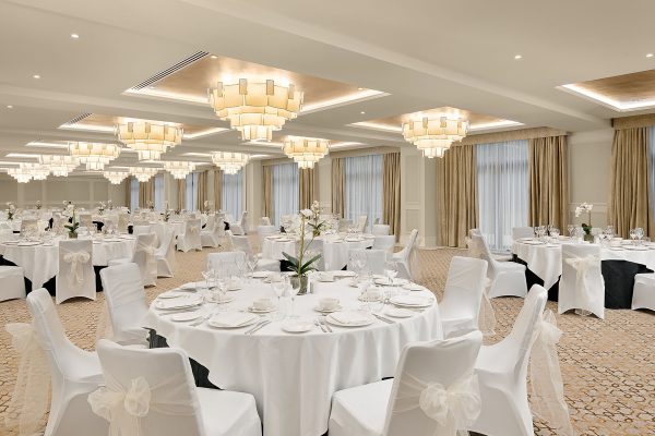 Monarch Suite ballroom at Fairmont Windsor Park with white table settings, chandeliers, and floor-to-ceiling drapes.