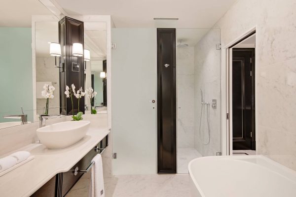 Luxurious bathroom at Fairmont Windsor Park with freestanding tub, glass-enclosed shower, and marble vanity.