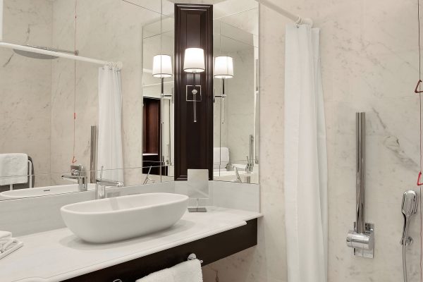 An accessible hotel bathroom at Fairmont Windsor Park with a roll-in shower, grab bars, and a modern vanity with a mirror.