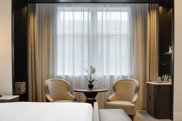 A bright and airy hotel room with a sitting area, sheer curtains, and a small table with an orchid at Fairmont Windsor Park.