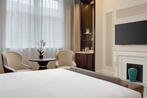 Stylish hotel room at Fairmont Windsor Park featuring a king-sized bed, a fireplace, a minibar, and a cosy seating area.