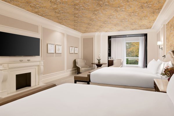 A deluxe hotel suite with two king beds, elegant lighting, and soft beige tones at Fairmont Windsor Park.