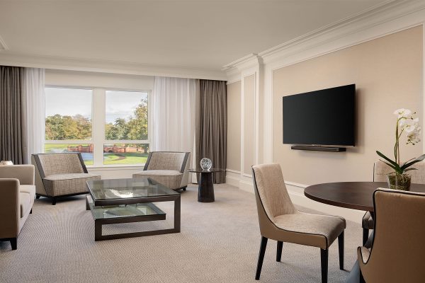 Stylish suite living area at Fairmont Windsor Park with plush seating, glass coffee table, and scenic pond view.