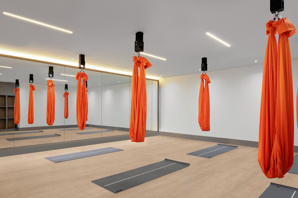 A well-lit aerial yoga studio at Fairmont Windsor Park featuring suspended orange aerial silk hammocks and mirrored walls.