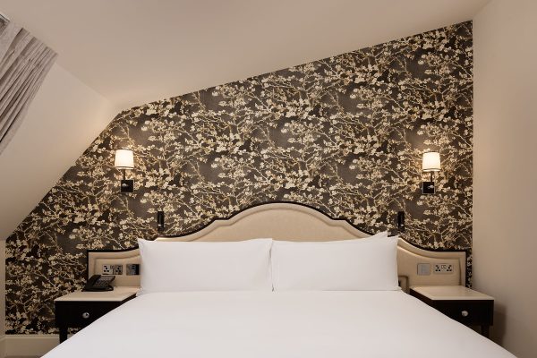 Cosy Eaves Queen room at Fairmont Windsor Park with dark floral wallpaper, warm lighting, and plush white bed.