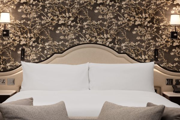 Close-up of plush bed and headboard with floral wallpaper and wall sconces at Fairmont Windsor Park.
