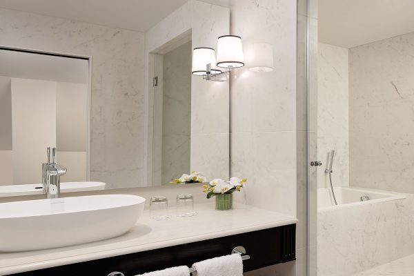 Luxurious marble bathroom at Fairmont Windsor Park with a sleek vanity, a large mirror, and a soaking bathtub.
