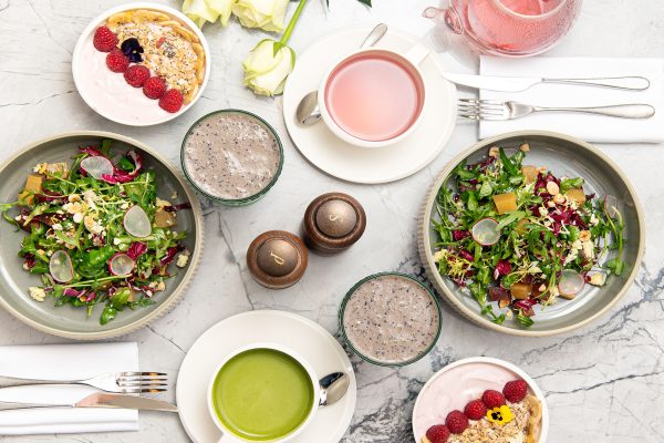 Healthy breakfast spread with fresh salads, yogurt with raspberries, matcha tea, chia pudding, and pink herbal tea.