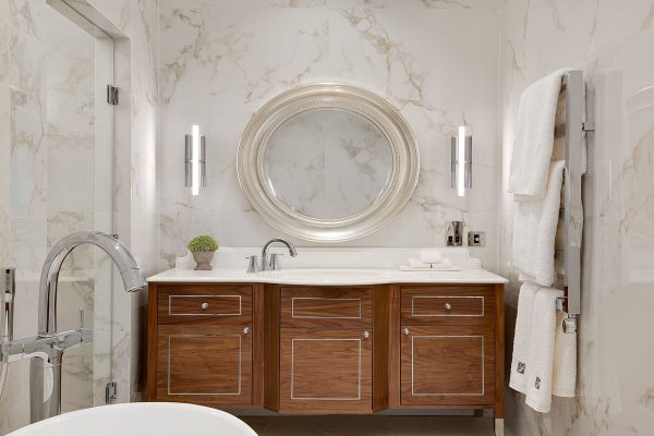 Sophisticated bathroom at Fairmont Windsor Park with marble walls, wooden vanity, round mirror, and modern lighting.