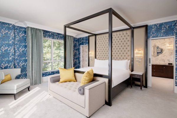A grand four-poster bed in the Royal Suite with blue floral wallpaper, and a cosy seating area at Fairmont Windsor Park.