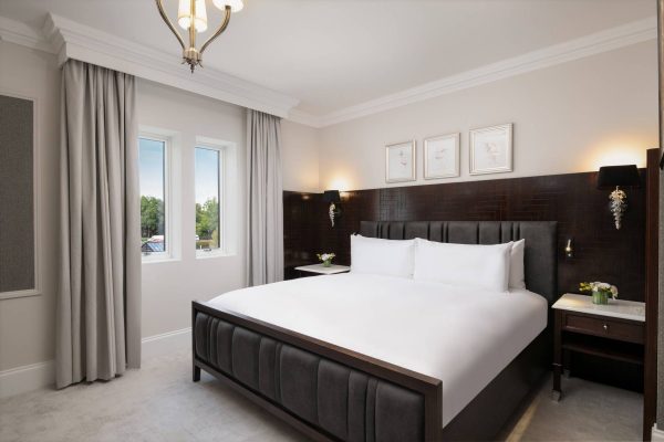 Stylish bedroom at Fairmont Windsor Park with king-size bed, dark wood accents, and framed bird illustrations.