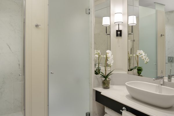 Elegant marble bathroom with sleek white sink, frosted glass shower, and fresh orchid decor at Fairmont Windsor Park.