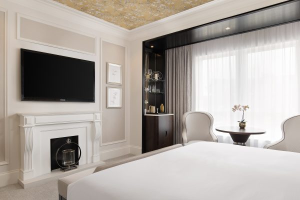 King Room at Fairmont Windsor Park featuring a fireplace, large TV, elegant decor, and a seating area with natural light from floor-to-ceiling windows.