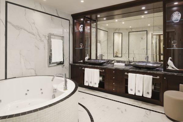 A marble-clad luxury bathroom at Fairmont Windsor Park featuring a jacuzzi, double vanity, and sleek dark wood accents.