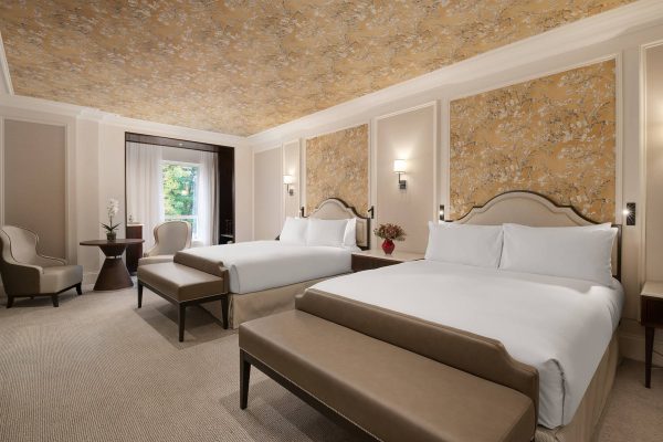 Refined twin suite at Fairmont Windsor Park with plush beds, gold floral wallpaper, and scenic window view.
