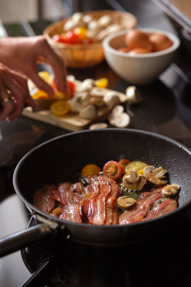 The Treehouse Suite Kitchen A woman cooking bacon, tomatoes and mushrooms on a frying pan