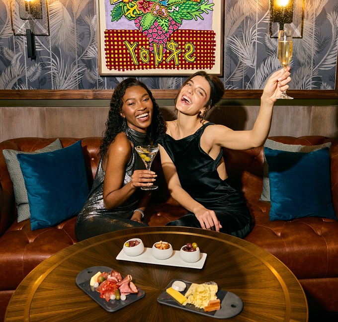 15-03546-M1-Final-1 Two female guests toasting with cocktails over charcuterie and cheese boards on the table at Bascule Bar, Cape Grace.
