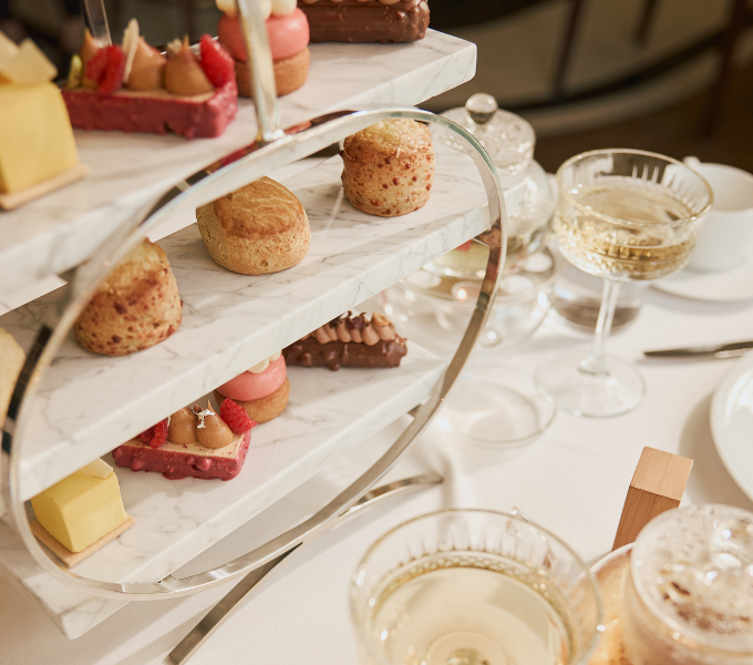 An elegant marble tiered afternoon tea stand showcasing cheddar scones, raspberry peaches and cream patisserie and gianduja chocolate cake alongside sparkling Cap Classique-filled glasses at Cape Grace, Cape Town.