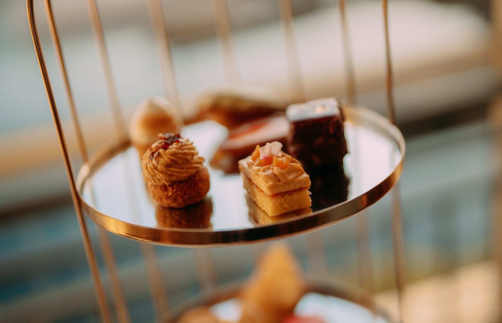 Close-up of handcrafted peaches and cream choux and vanilla cheesecake petit fours on the mirrored gold tier stand at Cape Grace Afternoon Tea, Cape Town.