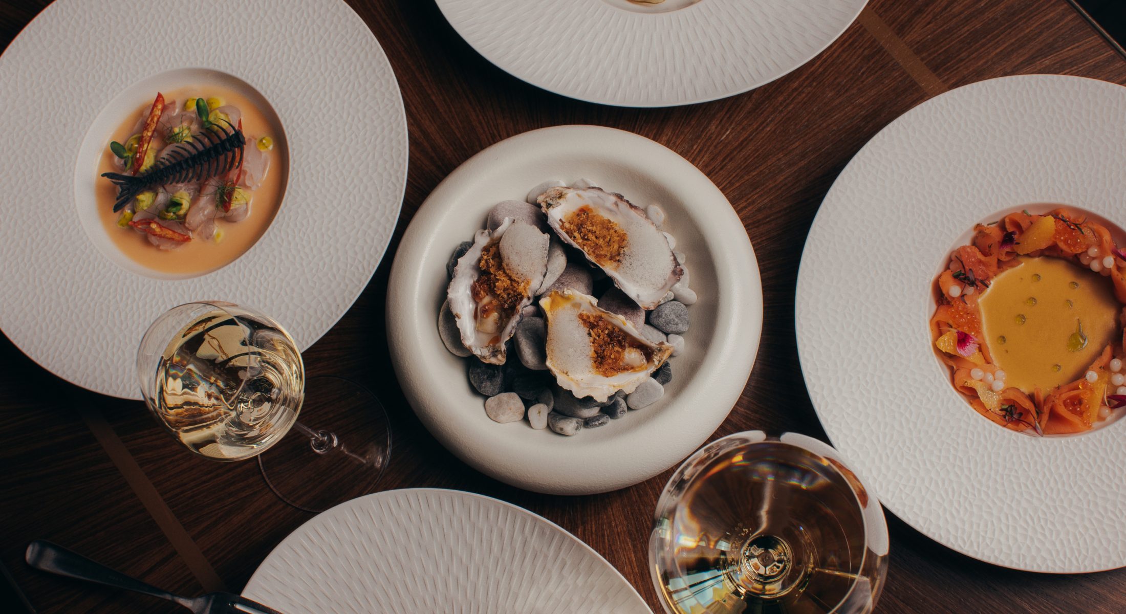 Top view of an elegant dining table with five gourmet dishes and two glasses of wine at Heirloom Restaurant, Cape Grace.