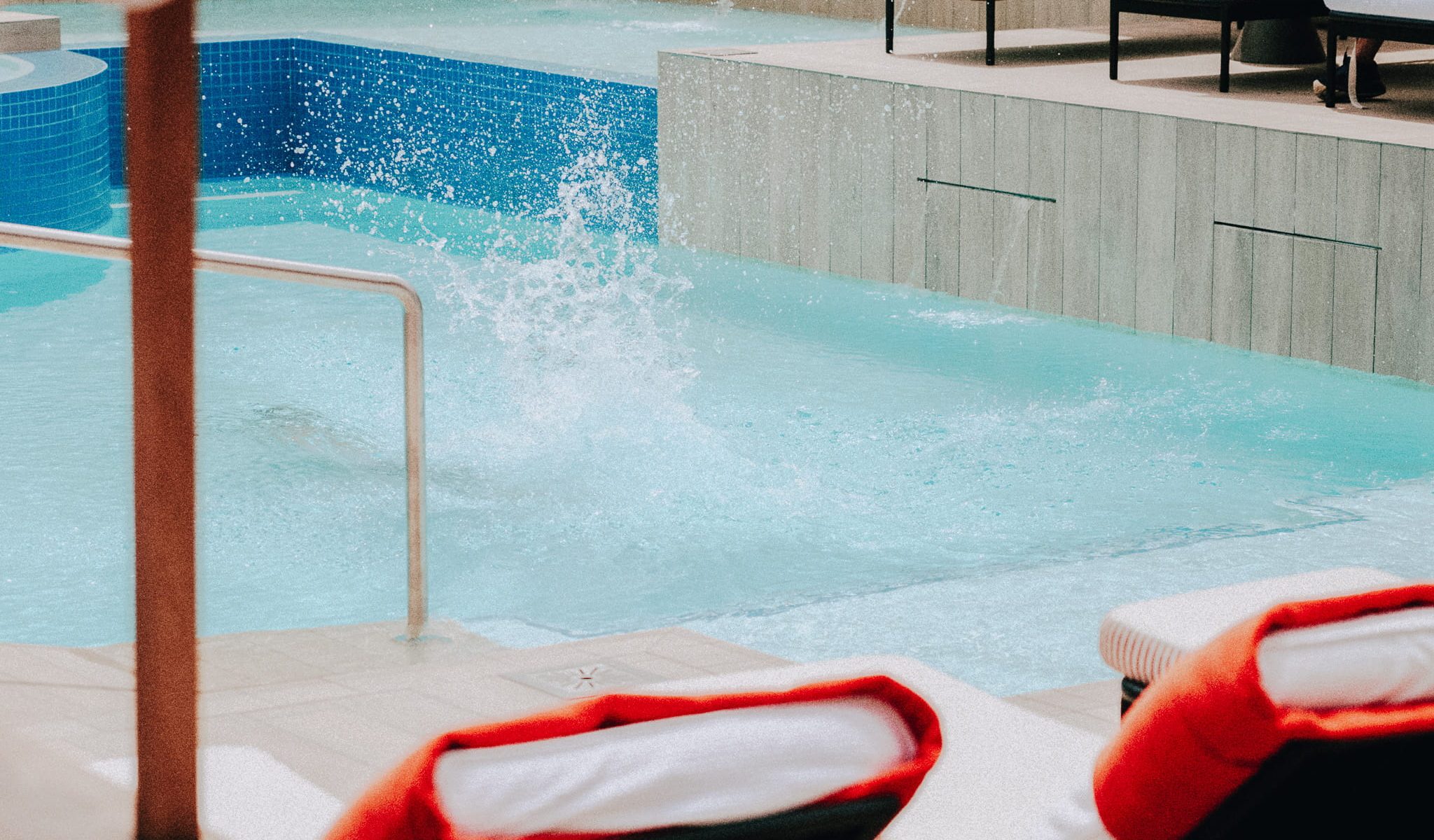 Heated outdoor pool with a splash, surrounded by cushioned loungers and warm, modern finishes at Cape Grace.