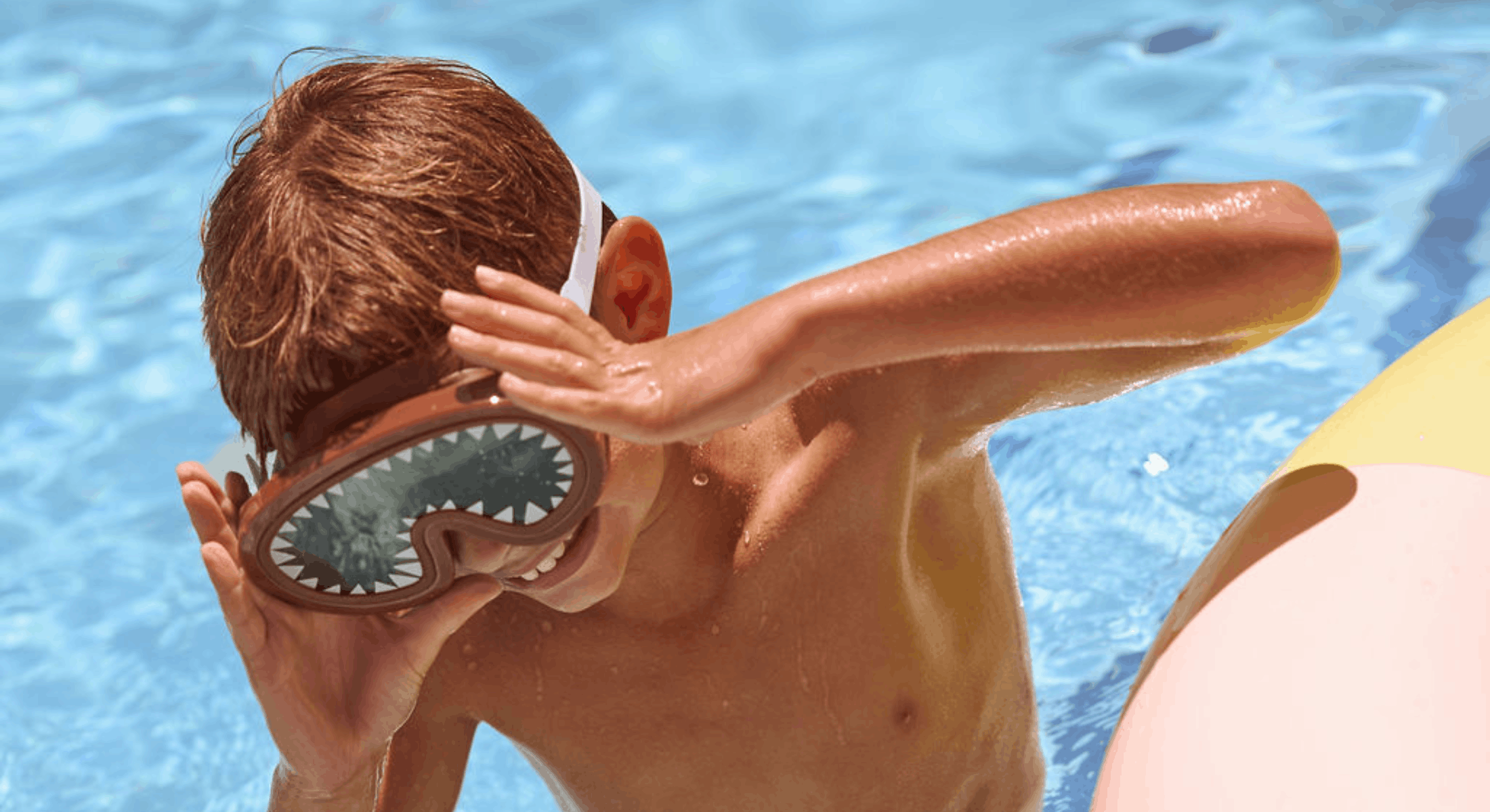 Young boy adjusting goggles while playing in a sunlit pool, enjoying a fun and carefree swim at Cape Grace.