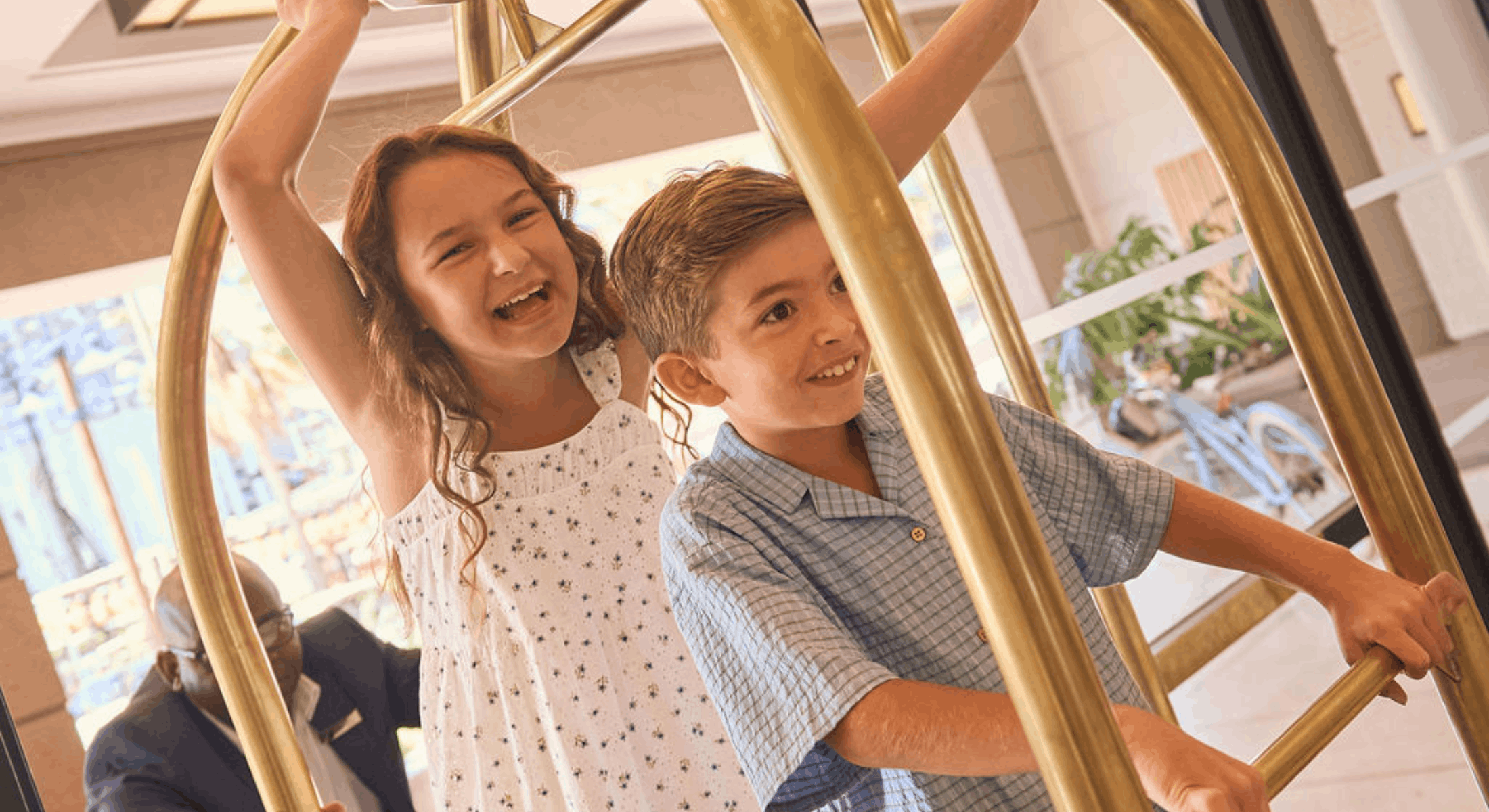 Happy children playing on a luggage trolley in the elegant Cape Grace lobby, enjoying a fun family moment.