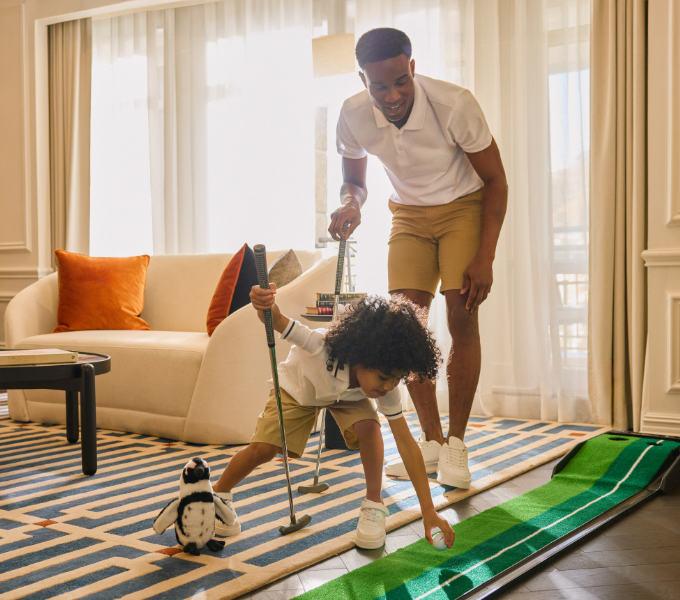 Parent and child playing mini golf together in a bright Cape Grace suite, showcasing playful in-room family experiences.