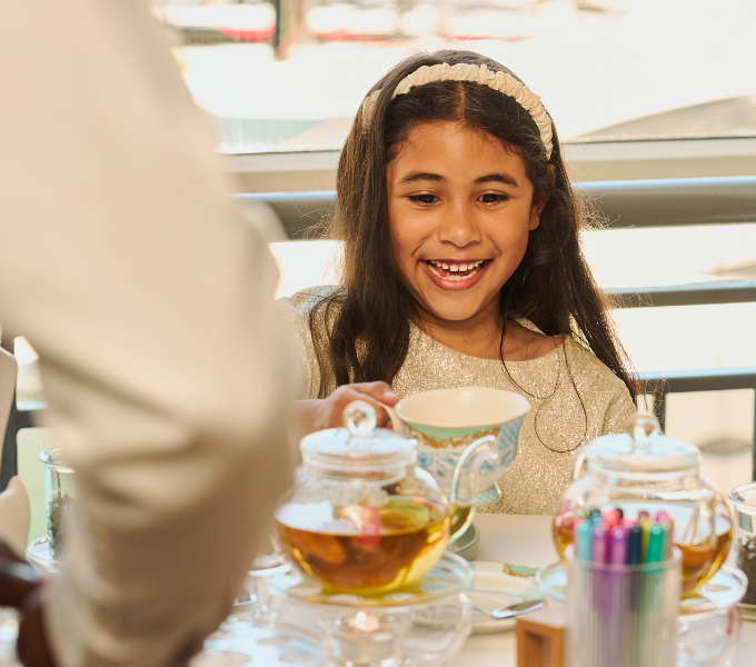 Young girl enjoying a Kiddies Afternoon Tea experience at Cape Grace, smiling over a beautifully set teacup and treats.