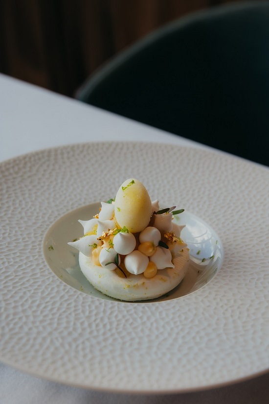 Elegant fine dining dessert with cream, citrus fruits, and meringue elements intricately plated on a textured white ceramic plate at Heirloom Restaurant, Cape Grace.